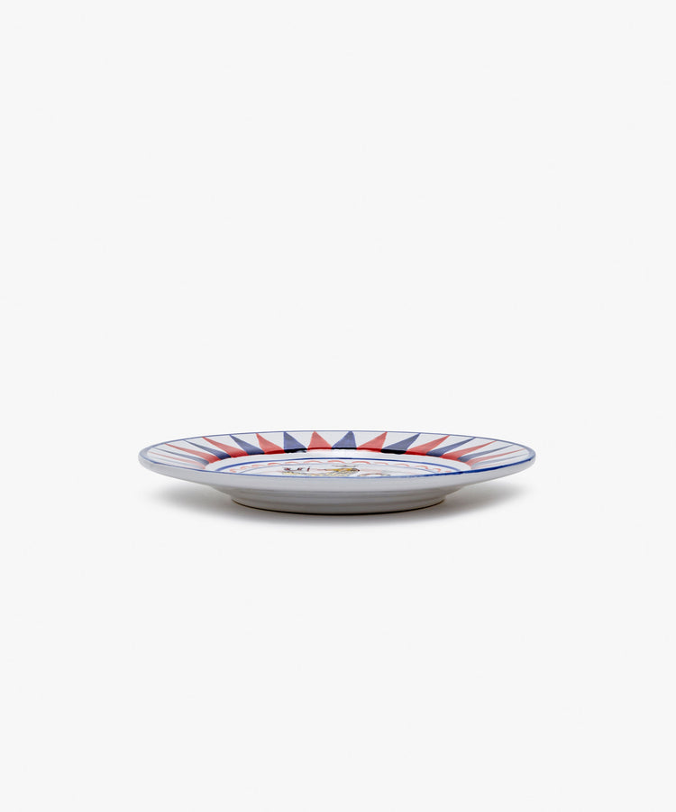 Palio Small Plate in white glazed ceramic with blue and red designs, side view.
