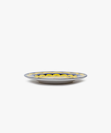 Palio Small Plate in white glazed ceramic with blue and yellow designs, side view.