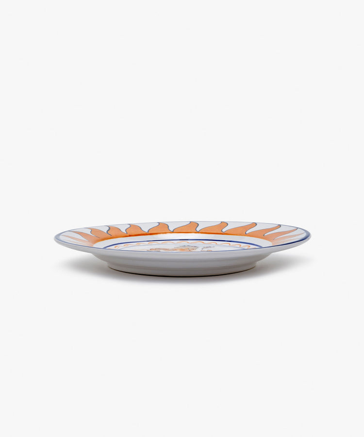 Palio Dinner Plate. Glazed ceramic in orange and navy designs with unicorn motif, angled side view.