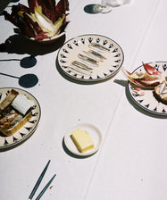 Tablescape with assorted plates and food on white tablecloth.