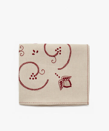 Inez Tablecloth. Folded cloth in tan cotton with red embroidered floral motif.
