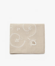 Inez Tablecloth. Folded cloth in tan cotton with white embroidered floral motif.