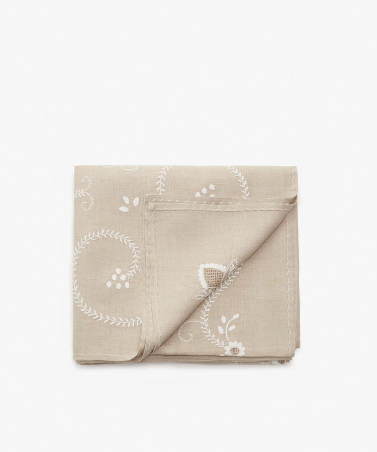Inez Tablecloth in tan cotton and white embroidery, folded with corner flipped up.
