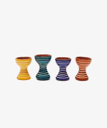 The Natalia Egg Cup, Set of 2, features handmade hourglass-shaped wooden cups with horizontal white stripes in yellow, green, blue, and red—perfect for serving classic egg and soldiers.