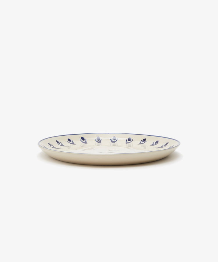 Vito Dinner Plate. White stoneware plate with painted blue rim and design details, side view.