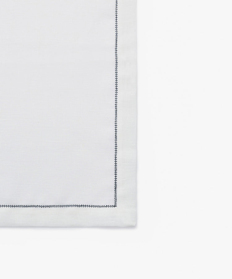 Close-up of dark blue stitching on white linen napkin.